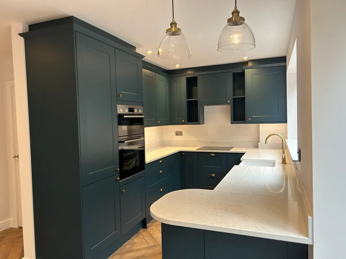 Deep blue shaker kitchen with a curved white peninsula, glass pendant lights and herringbone floor