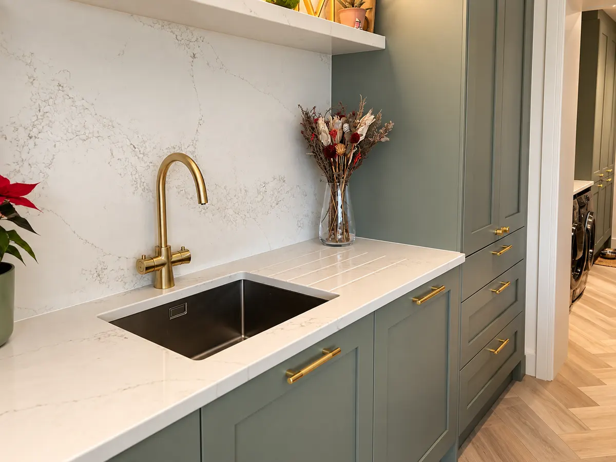 Close view of a stainless undermount sink, brass tap and brass bar handles on green shaker drawers